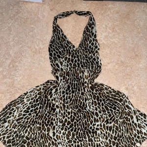 Leopardmönstrad långklänning med rosett - Säljer en snygg långklänning med leopardmönster och djup v-ringning. Klänningen har band som man kan justera runt midjan och är ärmlös med band som går back till nacken. 