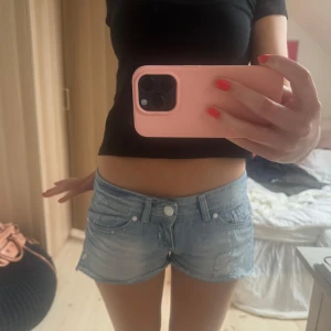 Ljusblå lågmidjade jeansshorts med slitningar - Säljer ett par ljusblå lågmidjade jeansshorts med slitna detaljer. Perfekta för varma dagar och enkel att matcha med olika toppar.