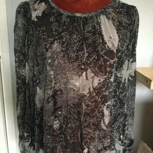 Mönstrad blus från Åhléns 38 - Säljer en tunn och luftig blus från Åhlens i svart, grått och vitt med abstrakt mönster. Blusen har rund halsringning och långa ärmar, perfekt för lager-på-lager. Passar till både jeans och kjol. Långärmad topp Åhléns Strl: 38. Katter finns i hemmet!