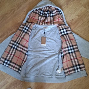 Burberry Hoodie - Säljer en grå hoodie från Burberry med dragkedja och två fickor framtill. Insidan av huvan har det ikoniska beige, svart och rödrutiga från Burberry. Såklart riktig dma för frågor!.