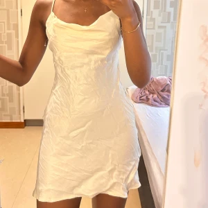 Beige satin klänning  - Säljer en vit kortklänning i satin från Tally Weijl. Klänningen har smala axelband, öppen rygg med snörning och en figurnära passform. Aldrig använd köpte i Italien för 2 år sen har bara legat i min garderob sen dess