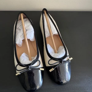 Svarta och vita ballerinaskor med rosett från Dasia - Snygga ballerinaskor från Dasia i svart och vitt med lackad tå och dekorativ rosett framtill. Skorna har rund tå och platt sula, samt guldfärgade detaljer på rosetten. Storlek 38 aldrig använda, nypris 1000 mitt pris 400, kan gå ner i pris vid snabb affär ❤️.