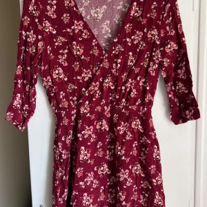 Vinröd blommig omlottklänning från H&M Divided - Säljer en vinröd omlottklänning från H&M Divided med små vita och rosa blommor. Klänningen har trekvartsärm, markerad midja och v-ringning. Perfekt för dig som gillar romantiska och feminina plagg. Nått slitage (se bild) men inget som syns eller stör när man har den på sig. Passar S (36) 