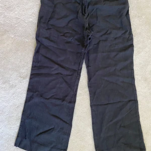 Svarta vida linnebyxor - Svarta linnebyxor med rak och vid passform. Byxorna har hög midja och är tillverkade i ett mjukt tyg som ger en avslappnad look. Perfekta för dig som gillar en loose och bekväm stil.