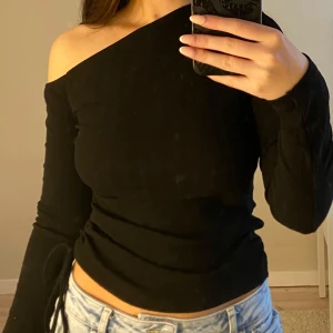 Svart oneshoulder topp med knyt - Svart oneshoulder topp med lång ärm och ribbad struktur från Gina Tricot. Toppen har snörning och knyt i sidan, använd ett fåtal gånger.
