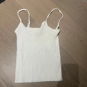 Vit ribbad linnetopp - Säljer en vit ribbad linnetopp med smala axelband. Toppen är enkel och stilren, perfekt att matcha med jeans eller kjol. Tillverkad i ett mjukt och stretchigt material som sitter skönt på kroppen.