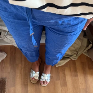 Blå linnebyxor med knytband - Säljer ett par blå linnebyxor med knytband i midjan. Byxorna har en avslappnad passform och är perfekta för varma dagar. De är raka i modellen och har en luftig känsla.