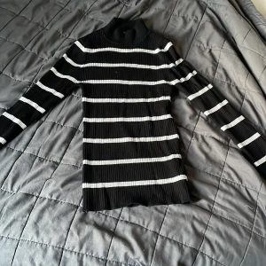 Svart och vit randig polotröja från Primark - Säljer en svart ribbad polotröja från Primark med vita horisontella ränder. Tröjan har lång ärm och är figurnära i modellen. Perfekt för lager-på-lager och enkel att matcha med jeans eller kjol.