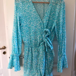 Blå blommig shortsdress  - Söt ljusblå shortsdress, som ser ut som en klänning, från FB Sister med vitt blommönster. Klänningen har långa ärmar med volang vid ärmslut och knyt i midjan. Super mjuk och skön att ha på sig! 🩵