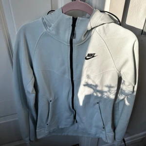 Ljusblå hoodiejacka från Nike - Säljer en ljusblå hoodiejacka från Nike med svart dragkedja och logga på bröstet. Jackan har huva med dragsko och två fickor framtill. Perfekt för en sportig och avslappnad stil. Helt ny aldrig använt! ❤️
