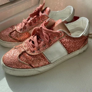 Glittriga sneakers från Valentino - Säljer ett par snygga sneakers från Valentino i rosa med glittriga partier och vita detaljer. Skorna har rosa snörning och en klassisk rund tå. Perfekta för dig som vill sticka ut med lite extra glitter i vardagen.