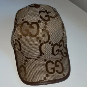 Gucci keps beige  - Säljer en beige keps från Gucci med brunt GG-mönster och bruna detaljer längs skärmen. Kepsen har klassisk form och är tillverkad i ett tygmaterial med tydlig logotypdesign. 