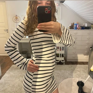 Vit och svart randig ribbad klänning från H&M - Kort, figurnära klänning i vit ribbad bomull med svarta horisontella ränder. Lapp borttagen men är från H&M i storlek XS. Långa ärmar som blir vida längst ut. Perfekt för en trendig och avslappnad look. Säljer eftersom jag aldrig använder klänningar.