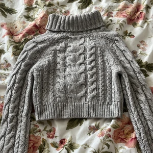 Grå stickad polotröja från Gina Tricot - Säljer en varm grå, croppad stickad polotröja från Gina Tricot. Tröjan är nästan oanvänd och säljs pga att den är för liten för mig. Tröjan har grova flätstickade mönster både fram och på ärmarna samt en hög, ribbad polokrage. Perfekt för kyliga dagar och enkel att styla till olika outfits. ❤️