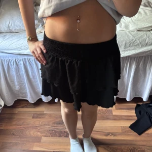 Svart volangkjol - Säljer en svart kortkjol med volangdetaljer och smock i midjan. Kjolen har en luftig och flowy känsla, perfekt för att styla med en crop top eller t-shirt. Enkel att matcha och superbekväm. Skriv för fler bilder💕 endast använd nån enstaka gång