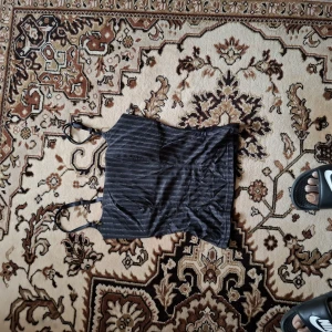 Svart linne med smala axelband och glittriga ränder - Säljer ett svart linne med smala axelband och tunna glittriga ränder. Toppen har en croppad passform och är perfekt för dig som gillar en stilren men ändå festlig look. Materialet är mjukt och stretchigt.