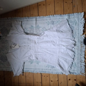 Vit kortklänning med volang och broderad spets - Superfin vit kortklänning från Sisters Point med volangdetaljer och broderad spets. Klänningen har v-ringning, korta ärmar och markerad midja. Perfekt för sommarens alla tillfällen!