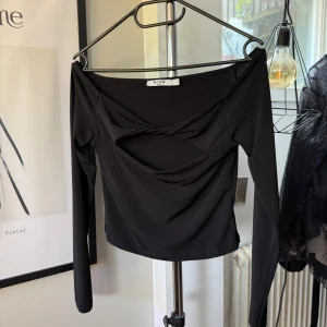 Svart långärmad topp med cut-out från NAKD - Trendig svart långärmad topp från NAKD med snygg cut-out detalj framtill. Toppen har en bred urringning och är i storlek S