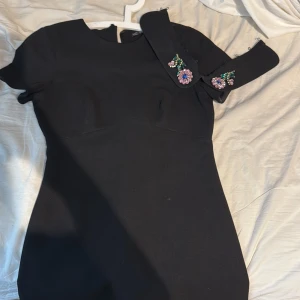 Svart klänning med broderad krage från Zara - Säljer en svart klänning från Zara med korta ärmar och en avtagbar krage dekorerad med broderade blommor och pärlor. Klänningen har en figurnära passform och dragkedja bak. Perfekt för dig som gillar unika detaljer! Den går ej att köpa i butik länge och är från Zaras Trafaluc Collection i storlek M. Den har använts ett par gånger men inget som syns. Klänningen når ner till knäna på ett ungefär. Köparen står för frakt 💗passar som vardag och enkel fest klänning 