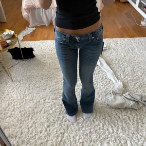 Blå bootcut jeans från True Religion - Säljer ett par  blå jeans från True Religion med bootcut-passform och låg midja. Köpta från Nelly för 1399kr. Sytt upp de ca 3 cm och faller över mina skor (är 160 cm) men aldrig använda samt lappen är kvar.