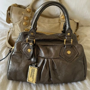 Bronze Q Classic Baby Groove väska! - Snygg bronze handväska i nyskick från Marc by Marc Jacobs i äkta läder med gulddetaljer och dubbla handtag. Lilla modellen Q Classic. Inga repor eller hål på väskans läder. Otroligt välbevarad vintage modell! Perfekt för att ge en stilren touch till din outfit. Skriv privat för fler bilder. Mått 34x18x12 (undersida). Kan hämtas hemma hos mig i Nacka eller skickas men kan tyvärr inte mötas🤍