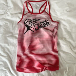 Röd- och vitrandig linnetopp från Wilson - Säljer en sportig linnetopp från Wilson med röda och vita ränder och tryck på bröstet. Perfekt för tennis eller träning. Topp med brottarrygg och lätt, luftig känsla. Den har röda fläckar på baksidan som knappt syns (se på 3 bilden).