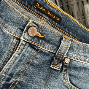 Blå jeans från Nudie Jeans Co - Säljer ett par klassiska blå jeans från Nudie Jeans Co med snygga kontrastsömmar och femficksdesign. Jeansen har slim fit passform, perfekt för en avslappnad stil. Märkets ikoniska broderi syns på bakfickorna.