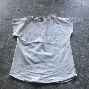 Vit t-shirt med text från Lindex - Vit t-shirt från Lindex med tryckt texten 'Wake up awesome' på framsidan. Klassisk rund halsringning och korta ärmar. Perfekt för en avslappnad stil.