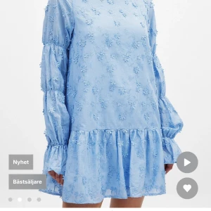 NA-KD. Oanvänd, tagg på.Blå blommig klänning med volang och öppen rygg - Söt ljusblå klänning med blommigt broderi, volang nertill och långa puffärmar. Klänningen har öppen rygg med knytband och en lös passform. Perfekt för vår och sommar!