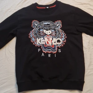 Svart sweatshirt med tigerbroderi från Kenzo - Säljer en svart sweatshirt från Kenzo i riktigt bra skick köpt på zalando, med det ikoniska tigerbroderiet och texten 'Paris' framtill. Perfekt för dig som vill sticka ut med en snygg och trendig look. använd ett fåtal gånger. 