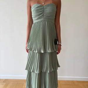Ljusgrön plisserad långklänning från Lulus - Säljer en ljusgrön axelbandslös långklänning från Lulus med plisserat tyg och volangdetaljer i flera lager. Klänningen har en romantisk och flowy siluett, perfekt för speciella tillfällen. Dragkedja i ryggen för enkel påklädning. Själv är jag 157 cm lång.  Byst:76,2-78,7 