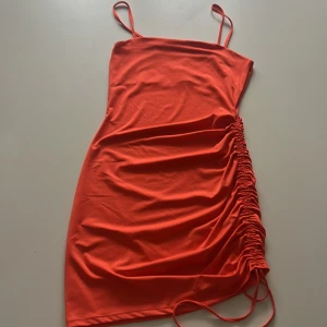 Orange omlottklänning från H&M Divided - Säljer en orange kortklänning från H&M Divided med smala axelband och snygg rynkdetalj med knyt på sidan. Klänningen har en figurnära passform och är tillverkad i mjuk polyesterblandning. Perfekt för dig som vill sticka ut! Aldrig använt🧡