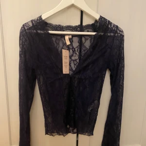 Blå spetsblus från Nelly - Säljer en elegant svart spetsblus från Nelly. Blusen har långa ärmar och en vacker spetsdesign som ger en romantisk känsla. Perfekt för att lägga till en touch av elegans till din garderob. 💫