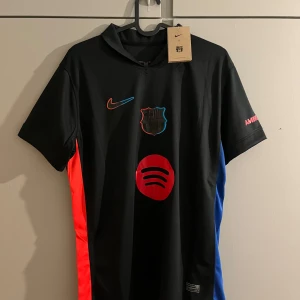 FC Barcelona svart matchtröja Raphinha 11 - Säljer en svart FC Barcelona fotbollströja från Nike med Raphinha 11 på ryggen. Tröjan har röda och blå detaljer på sidorna, klubbmärke och Nike-logga framtill samt Spotify-logga. Kortärmad modell med 'AMBILIGHT' på ärmen.