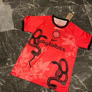 Inter Milan röd bortatröja med ormtryck - Säljer en röd Inter Milan fotbollströja från Nike med svart ormtryck och blommönster. Tröjan har svart krage och svarta ärmslut samt klubbmärke och sponsorlogga på bröstet. Perfekt för dig som vill sticka ut på planen.