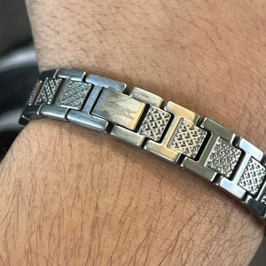 Lacoste Silverfärgat armband i rostfritt stål - Snyggt armband i silverfärgat rostfritt stål med rektangulära länkar och dekorativa mönster. Armbandet har en stilren och maskulin design, perfekt för att lyfta din outfit. Länkarna har både släta och mönstrade ytor för extra detalj.