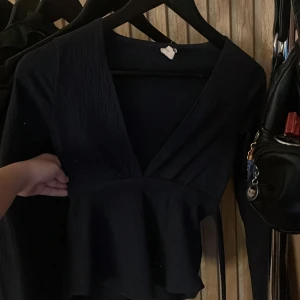 Svart omlottopp från Nelly - Säljer en marinblåomlottopp från Nelly i storlek XXS. Toppen har långa ärmar, markerad midja och volang nedtill. Perfekt att styla med jeans eller kjol för en snygg look.