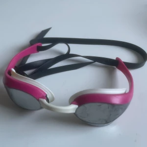 Rosa och vita simglasögon från Arena - OBS + 50kr för att få med ett hårt fodral med stor Arena-logga på locket (alltså 250 för båda och 200 för endast glasögonen) Snygga simglasögon från Arena i rosa och vitt med svarta band. Spegelglas och låg profil, perfekta för simträning. Säljer då jag inte simmar längre, nypris är 849kr. Pris kan diskuteras.