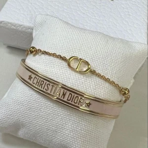 Armband från Christian Dior i guld och rosa - Säljer två snygga armband från Christian Dior. Ett är ett kedjearmband med CD-logga i guld och det andra är ett stela armband i guld och ljusrosa med texten CHRISTIAN DIOR och stjärndetaljer.