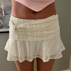 Vit virkad kortkjol med volang - Superfin vit virkad kortkjol med volangkant och omlott-detalj i midjan. Kjolen har en söt och somrig vibe, perfekt till varma dagar. Den är stretchig och sitter bekvämt i midjan.