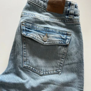 Ljusblå bootcut jeans - Säljer ett par ljusblå jeans med bootcut passform och klassiska bakfickor med knapp. Jeansen har normal midja och är tillverkade i denim. Perfekta för dig som gillar en avslappnad och tidlös stil. Original pris: 599kr