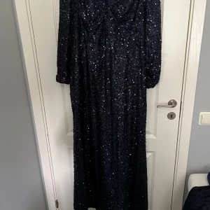 Mörkblå glittrig långklänning - Säljer en mörkblå långklänning med glittriga paljetter. Klänningen har långa ärmar och en elegant, figurnära passform. Perfekt för festliga tillfällen när du vill sticka ut och glänsa.
