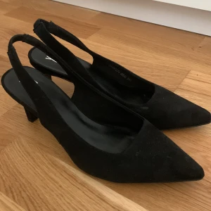 Svarta pumps med öppen häl  - Stilrena svarta pumps med spetsig tå och öppen häl i storlek 37. Skorna har en låg klack och är tillverkade i ett mockaliknande material. 🤗🌸