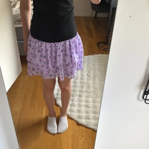 Ljuslila blommig volangkjol - Supersöt ljuslila kjol med små blommor och volanger. Kjolen har smock i midjan för en bekväm passform och är kort i modellen. Perfekt till sommaren.