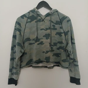 Grön camo hoodie - Säljer en croppad hoodie från Gina Tricot i grönt camouflage-mönster. Tröjan har huva med dragsko och muddar vid ärmslut. Perfekt för en avslappnad streetstil.