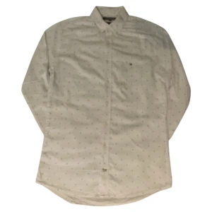 Vit skjorta med ankarmönster från Tommy Hilfiger - Säljer en vit långärmad skjorta från Tommy Hilfiger med små bruna ankare som mönster. Klassisk krage och knäppning framtill. Perfekt för dig som gillar stilrena detaljer och marint tema. Märkets logga broderad på bröstet.