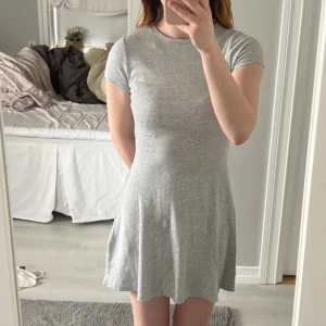 Ljusgrå kortklänning - Superenkel och snygg ljusgrå klänning. Modellen är figurnära upptill och har en lätt utställd kjol. Aldrig använd!