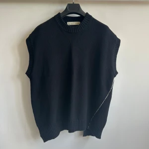 Svart stickad väst Adnym - Säljer en svart stickad väst från Adnym med grov ribbstickad halsringning och nederkant. Västen har en asymmetrisk form och en diskret söm som löper snett över plagget. Generös oversized passform som passar någon som vanligtvis bär S-L. Påminner om Ann Demeulemeester, Rick Owens, Yohji Yamamoto, Comme des Garcon, Undercover