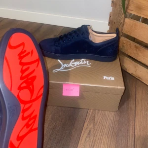 Christian Louboutin skor - Säljer ett par mörkblå sneakers från Christian Louboutin med klassisk röd sula. Skorna har snörning och är tillverkade i mocka. Perfekta för dig som vill sticka ut med exklusiva detaljer och snygg design. OBS* Skorna är i storlek 43