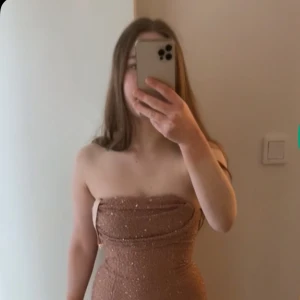 Glittrig champagnefärgad långklänning från Oh Polly - Säljer en snygg axelbandslös långklänning från Oh Polly i champagnefärg med glittriga detaljer. Klänningen har en tight passform och är perfekt för festliga tillfällen. Materialet är stretchigt och sitter smickrande på kroppen.